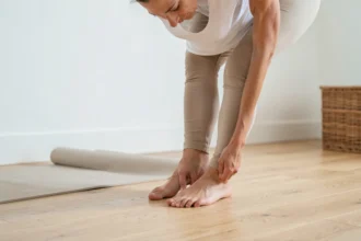 Femme debout pieds nus montrant un pied égyptien avec le deuxième orteil plus long, observant sa posture dans un intérieur minimaliste